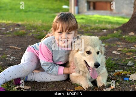 Portrait of a young blond girl child cuddling white puppy outdoors in the park Stock Photo