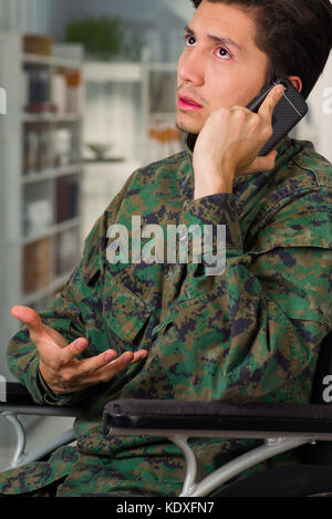 Portrait of a handsome young soldier sitting on wheel chair using his cellphone, in a blurred background Stock Photo