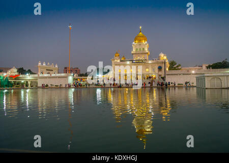 DELHI, INDIA - SEPTEMBER 19, 2017: Unidentified people walking in front of the main Sikh shrines of Delhi - Gurudwara Bangla Sahib. The main building of the temple is illuminated and is reflected in Sarowar pond water in India. Stock Photo