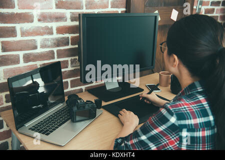 back view of professional young female photo designer transport photographer picture into computer and using digital pen editing retouch in business o Stock Photo