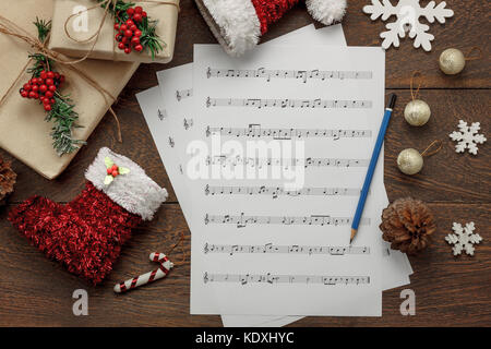 Aerial view of Merry Christmas and music background concept.Essential decorations & ornament with paper white notes.Objects on brown modern rustic tab Stock Photo