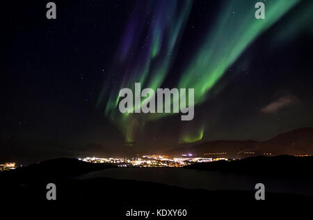 Aurora Borealis with shining stars on the sky over the mountains and highlighted city, Nuuk, Greenland Stock Photo