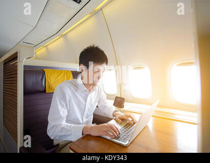 Asian man using laptop on luxury airplane Stock Photo