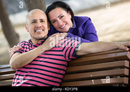 Senior happy couple sitting together on the bench and holding each other Stock Photo