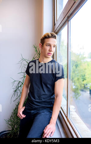 A handsome young man standing beside the window. Stock Photo