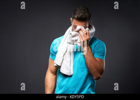 A handsome young sportsman feeling tired and wiping his face with a towel Stock Photo