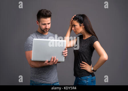 A handsome young man holding a laptop next to his girlfriend who is feeling upset Stock Photo