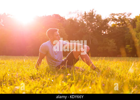 A handsome young man relaxing in the sunset and sitting in the grass. Stock Photo