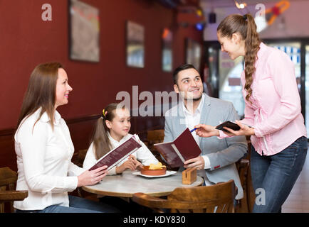 smiling waitress and happy family with child reading menu. Focus on the waitress and woman Stock Photo