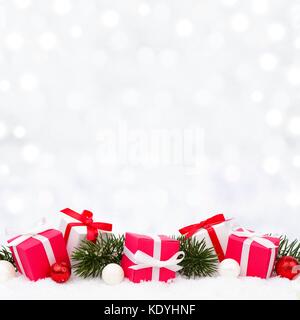 Red and white Christmas gifts in snow with branches and twinkling silver background Stock Photo