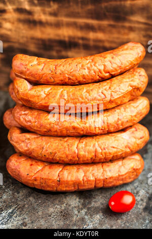 Stack of deliciously smoked handmade Swedish Isterband sausages with natural casing. Here with a tomato. Stock Photo