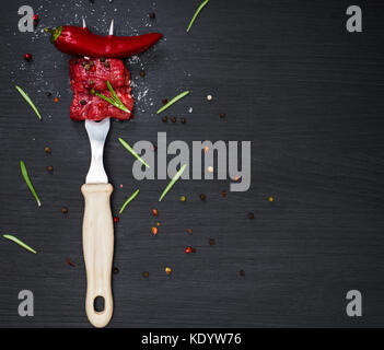 two pieces of beef and red chili pepper strung on a kitchen plug on a black background, empty space on the right Stock Photo