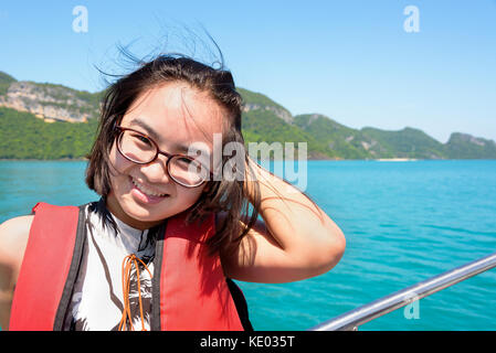 Cute young woman with eyeglasses smiling happily on the boat while cruising the beautiful natural of the blue sea and sky in summer at Mu Ko Ang Thong Stock Photo