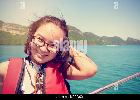 Vintage style young woman with eyeglasses smiling happily on the boat while cruising the natural of the sea and island in summer at Mu Ko Ang Thong Na Stock Photo