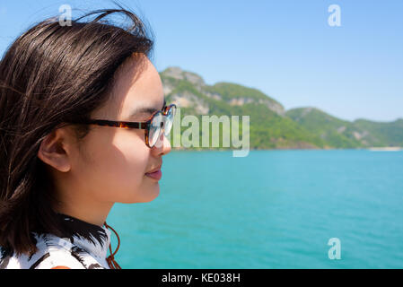 Cute young woman with eyeglasses smiling happily on the boat while cruising the beautiful natural of the blue sea and sky in summer at Mu Ko Ang Thong Stock Photo