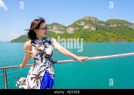 Asian young woman with eyeglasses smiling happily on the boat while cruising the beautiful natural of the blue sea and sky in summer at Mu Ko Ang Thon Stock Photo