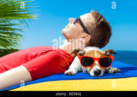 jack russell dog  and owner sunbathing a having a siesta under a palm tree , on summer vacation holidays at the beach Stock Photo