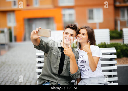 Handsome young couple sitting on the bench in the center of the city and taking a selfie .Love and tenderness. Lifestyle concept Stock Photo