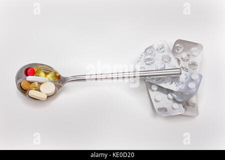 Silver spoon full with colorful pills on top of used tablet blisters Stock Photo