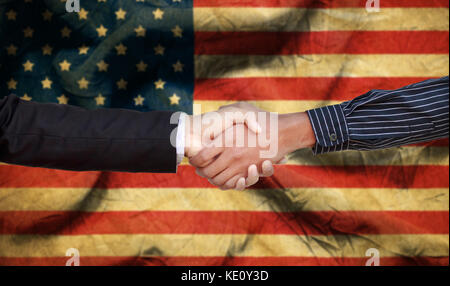 International Handshake with white and dark skinned businessman on background of the USA flag. Stock Photo