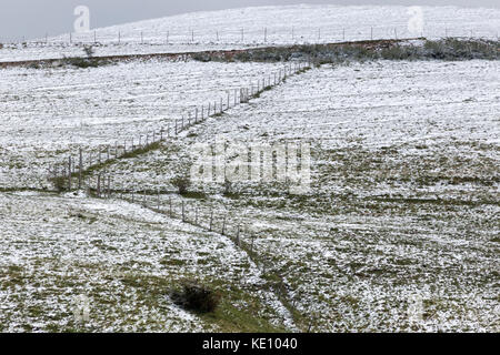A fence running up on a mountain, in the midst of snow covering partially the grass meadows Stock Photo