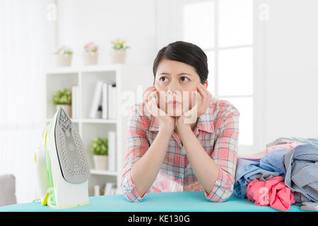 pretty elegant housewife ironing clothing feeling boring and leaning on board thinking how to fast doing housework method. Stock Photo