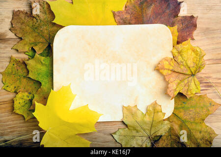 Old grunge paper page over fall leaves on wooden table Stock Photo