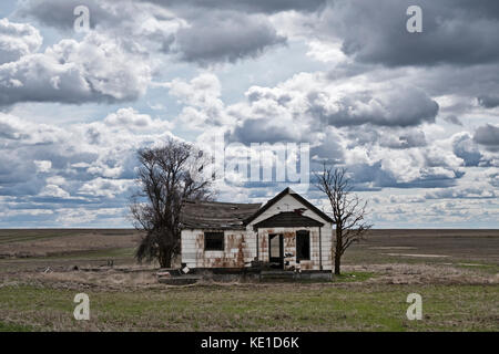 An old farmhouse homestead stands isolated and abandoned amid an empty and endless field in the Palouse area of Eastern Washington as seen on a cloudy Stock Photo