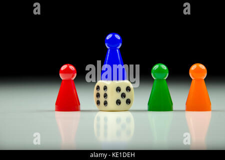 Close-up view of a row of colored figures and playing cube with blurred black and white background with reflection Stock Photo