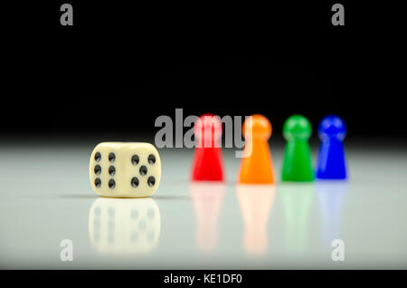 Close-up view of a row of colorful figures at the back with a playing cube on a blurred white-black background with reflection Stock Photo