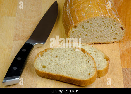 Close-up photo of two slices of bread cut by knife with black handle on a wooden board table with blurred background Stock Photo