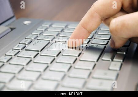 Closeup view of a hand with a finger press the Enter key on the silver keyboard laptop lying on a wooden mat blurring Stock Photo