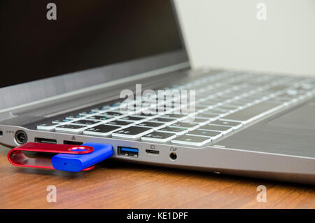Close-up view of a silver laptop with attached blue flash disk on a wooden table and on a white background Stock Photo