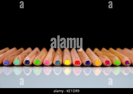 Close-up view of colored pencils lying on glossy white background with reflection isolated on black background Stock Photo