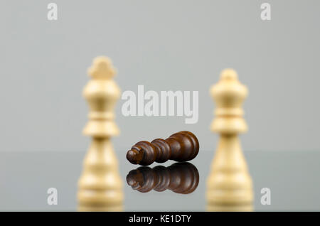 Close-up view of two wooden white chess pieces defeating a black chess king with a reflection in the glass Stock Photo