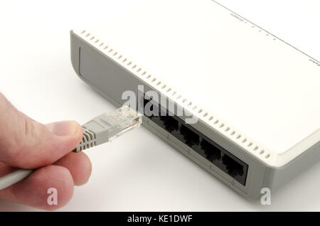 A close-up view of a finger's hand connecting a gray lan cable into the router on a white background Stock Photo