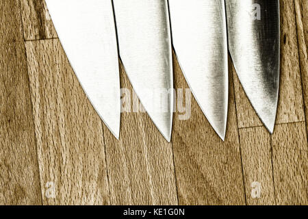 Four identical kitchen knives on a wooden work top Stock Photo