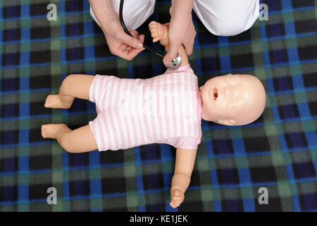 Infant first aid series - First aid instructor showing how to check pulse on infant dummy using stethoscope Stock Photo