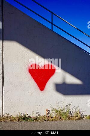 red heart shaped gaffitti painted on white textured wall Stock Photo