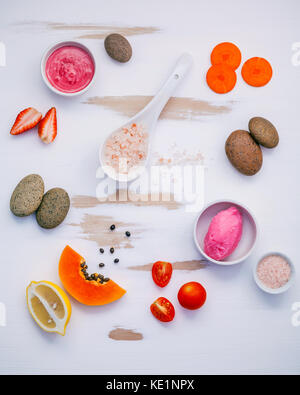 Homemade skin care and body scrubs with red natural ingredients strawberry , tomato ,himalayan salt, ripe papaya, carrot and spa stone setup on white  Stock Photo
