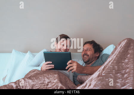 Happy couple, husband and wife in bedroom using personal electronics devices Stock Photo