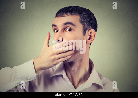 Headshot of a scared adult man with hand covering his mouth isolated on gray wall background Stock Photo