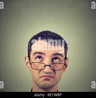 Closeup funny confused skeptical man in glasses thinking planning looking up above head isolated gray wall background copy space. Human face expressio Stock Photo
