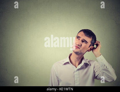 Closeup portrait man scratching head, thinking deeply about something, looking up, isolated on grey wall background. Human facial expression, emotion, Stock Photo