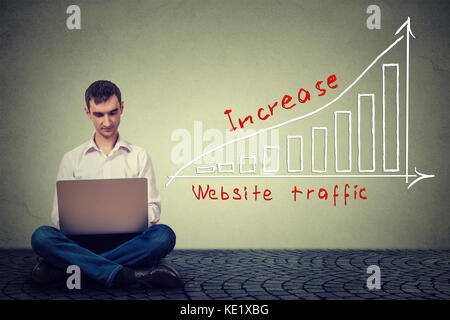IT guy young man using laptop sitting on a floor working on a plan to increase website traffic. Technology marketing concept Stock Photo