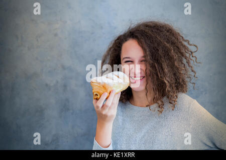 Portrait of curly hair teen girl holding fresh croissant Stock Photo