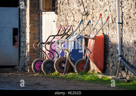 colorful wheelbarrows against stone wall outside stable Stock Photo