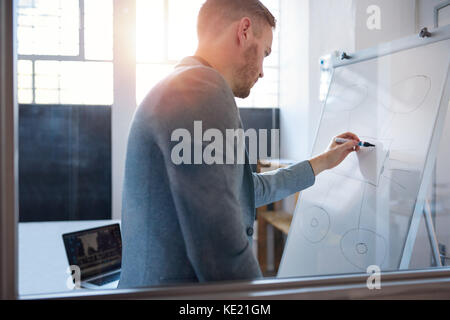 Young businessman writing on a whiteboard during an afternoon presentation to colleagues in the meeting room of a modern office Stock Photo