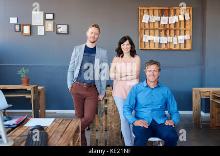 Portrait of three casually dressed work colleagues smiling confidently together while working in a large modern office