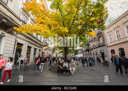 BELGRADE, SERBIA - OCTOBER 14, 2017: People having a break on a bench under a tree wearing autumn colors on Kneza Mihailova, the main pedestrian stree Stock Photo